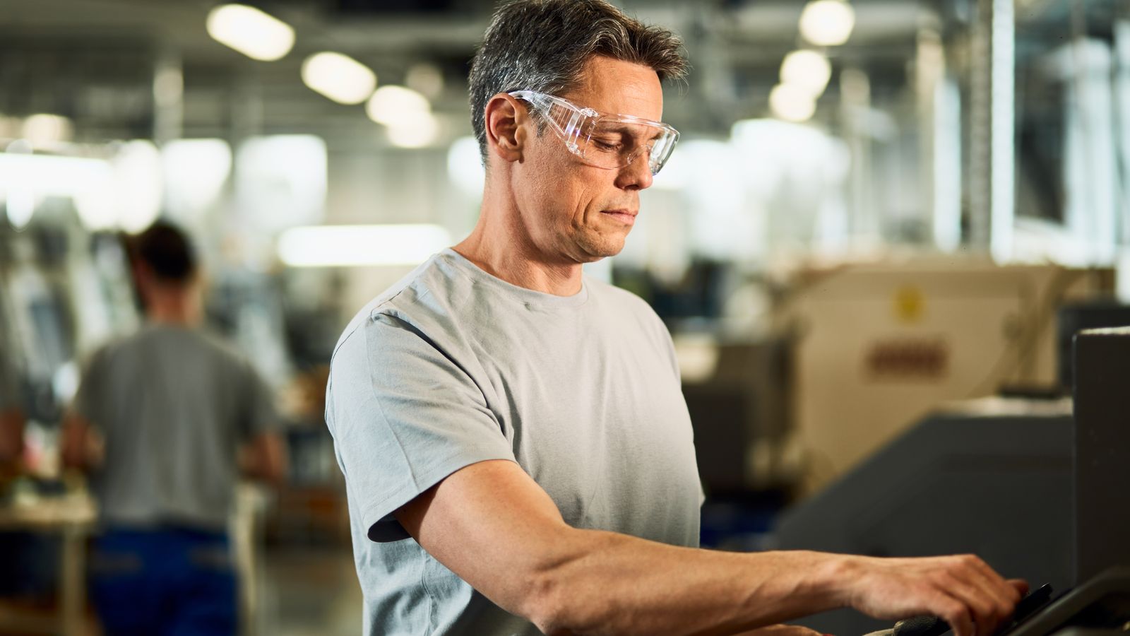 Operador de óculos de proteção ajustando uma máquina CNC na linha de produção